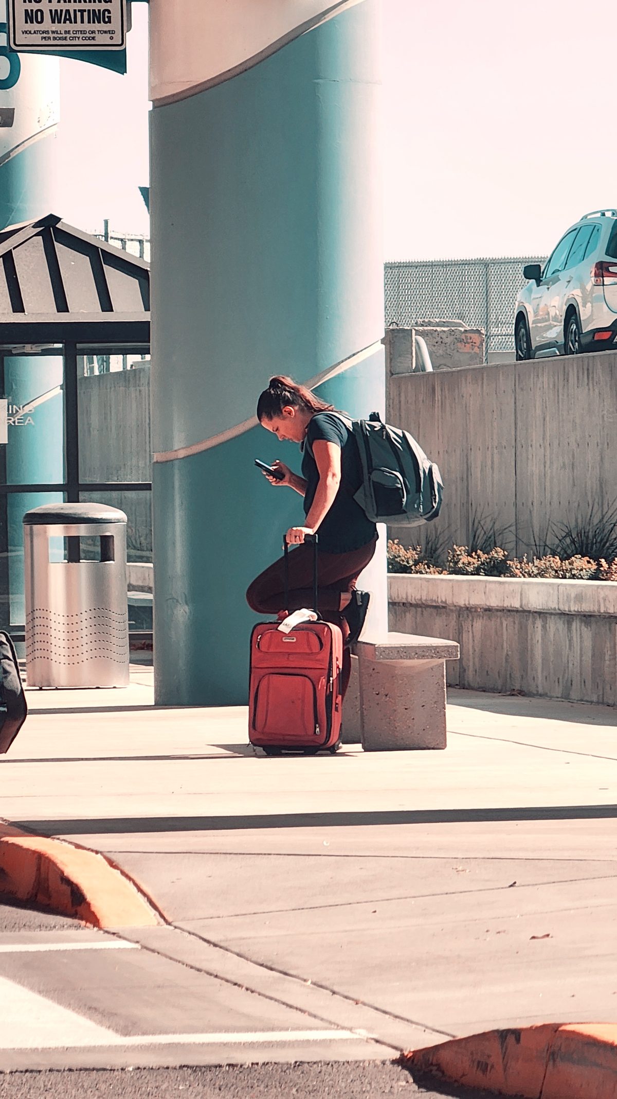 A traveler sitting on luggage at an airport curb