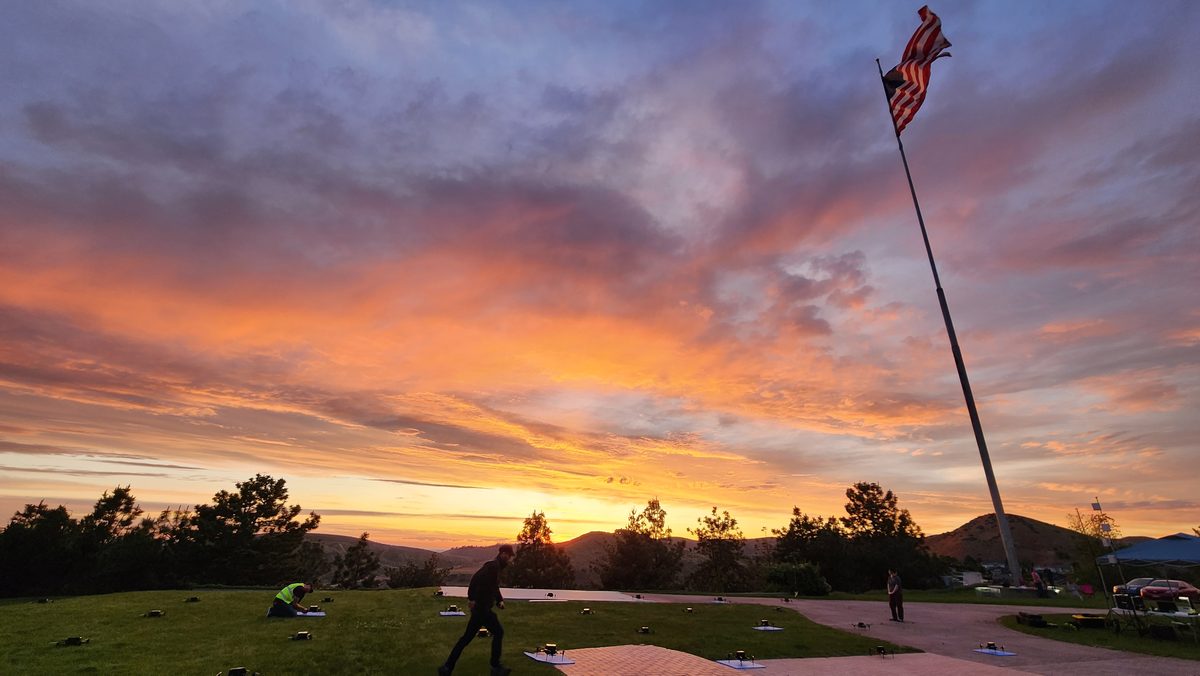 An American flag on a tall pole against a vivid orange and purple sunset over a lawn