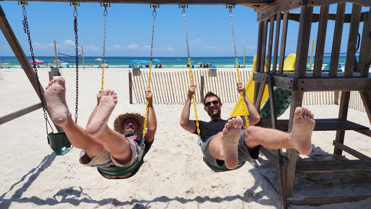 Two friends laughing on swings at a sunny beach