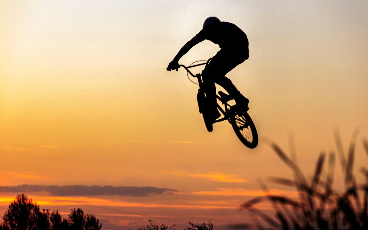 Silhouette of a BMX rider in mid-air against an orange sunset sky