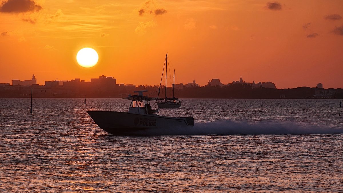 A small boat speeding across the water under a huge orange setting sun