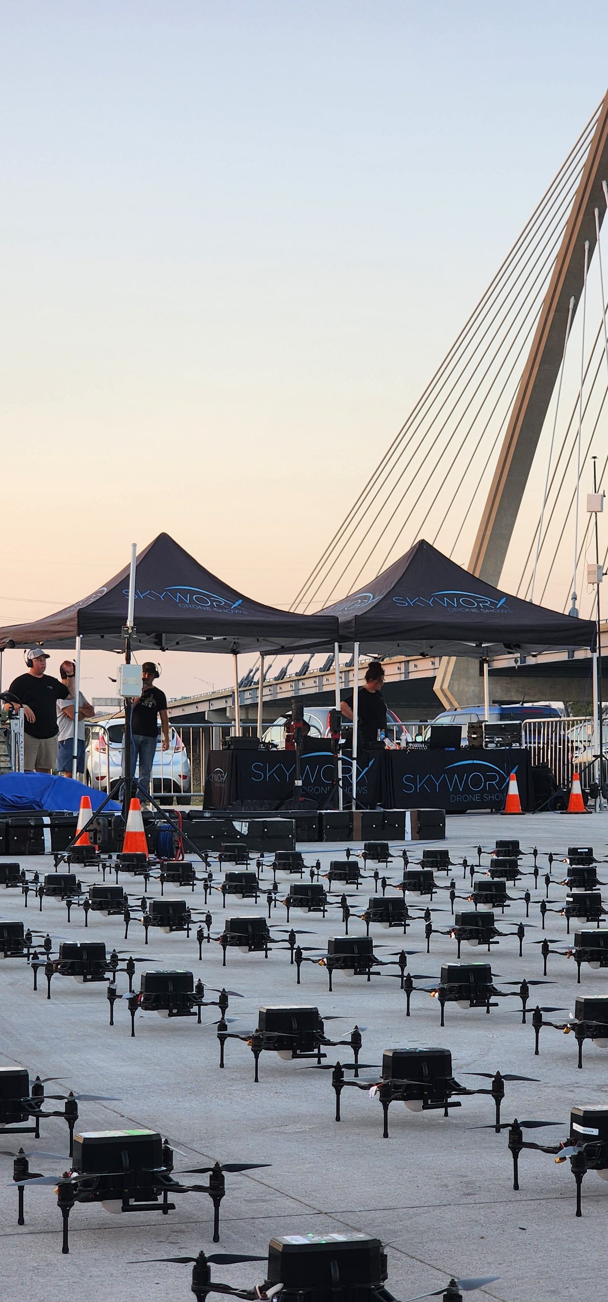 A cable-stayed bridge mast above event tents and seating