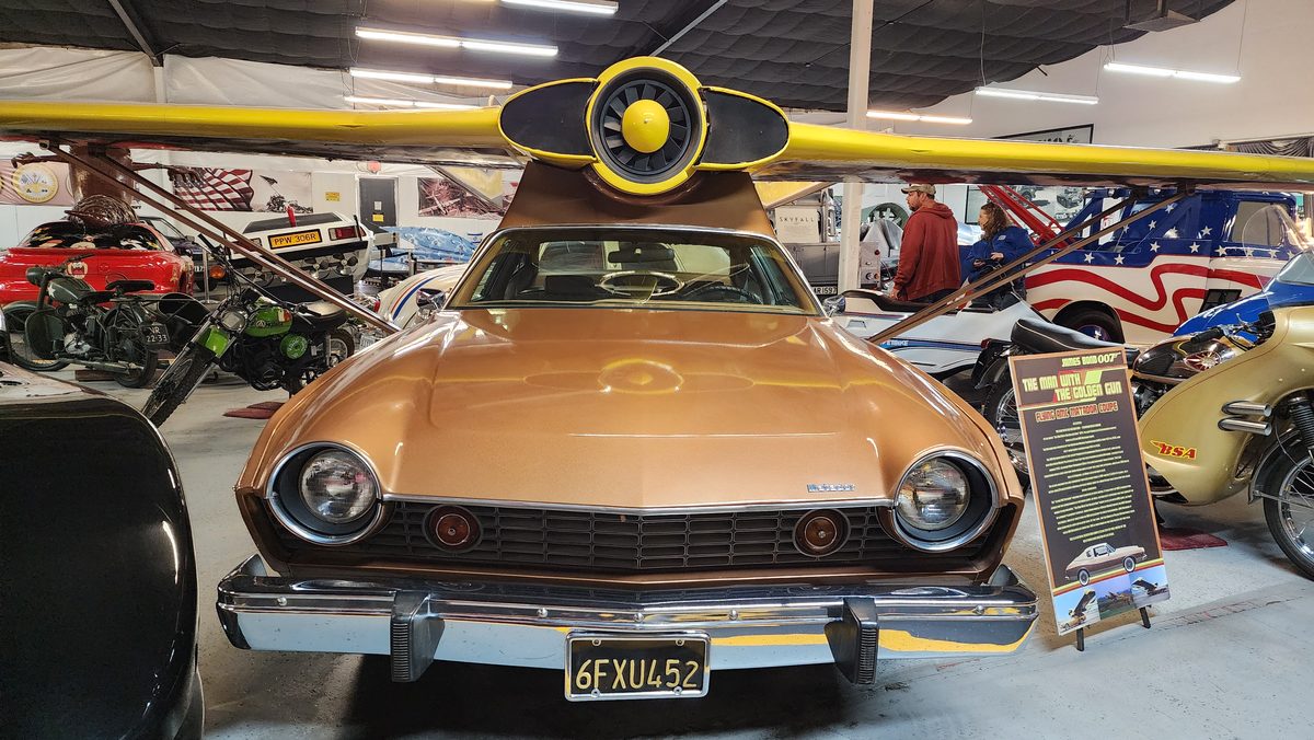 A gold classic car with airplane-style wings at a car museum