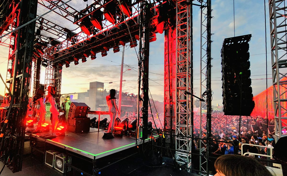 An outdoor concert stage and speaker towers glowing red at dusk