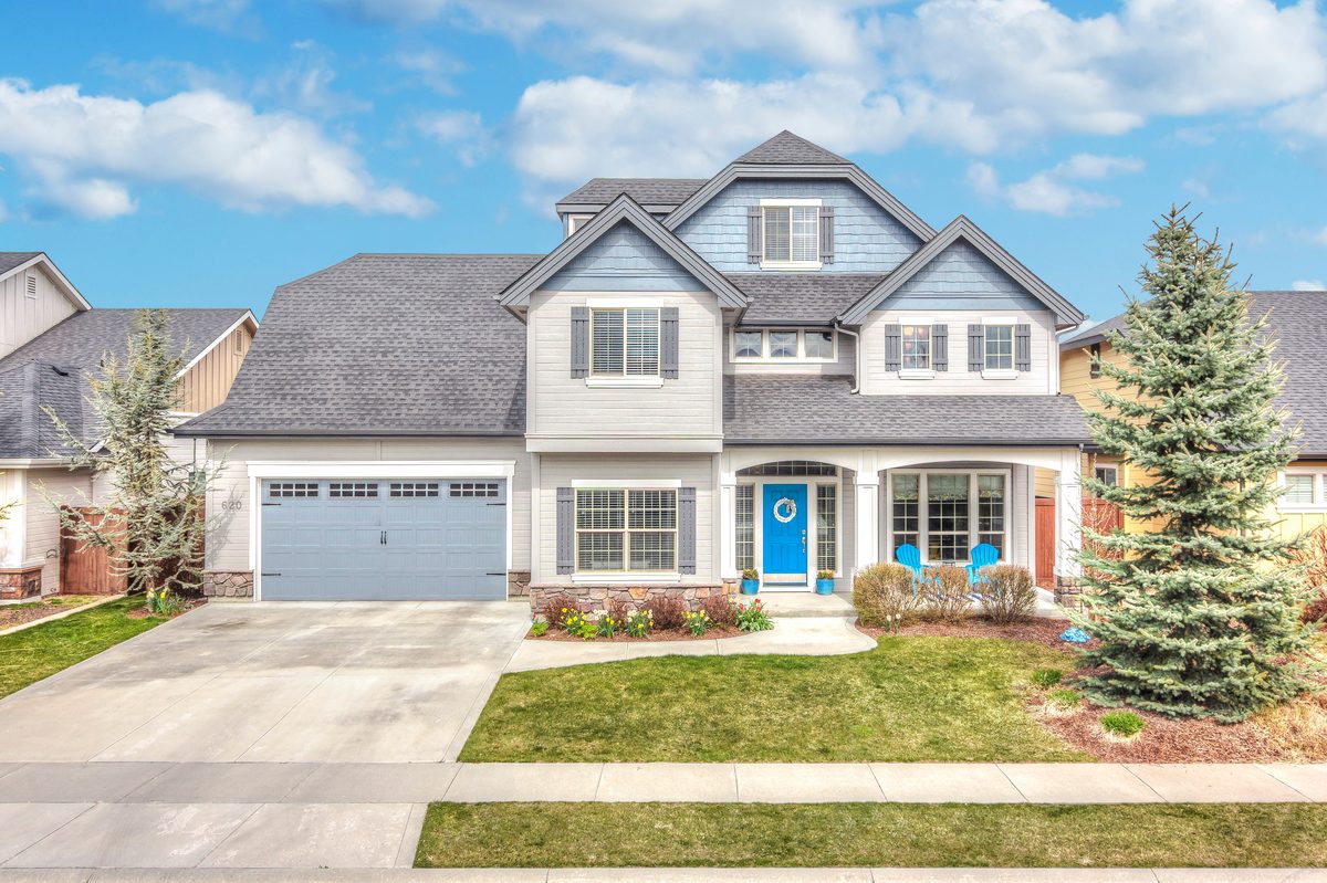 Two-story craftsman-style home with a gray garage door and landscaped front yard