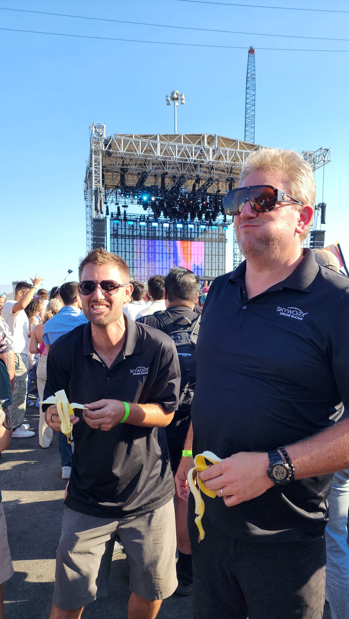 Two crew members laughing in front of an outdoor concert stage