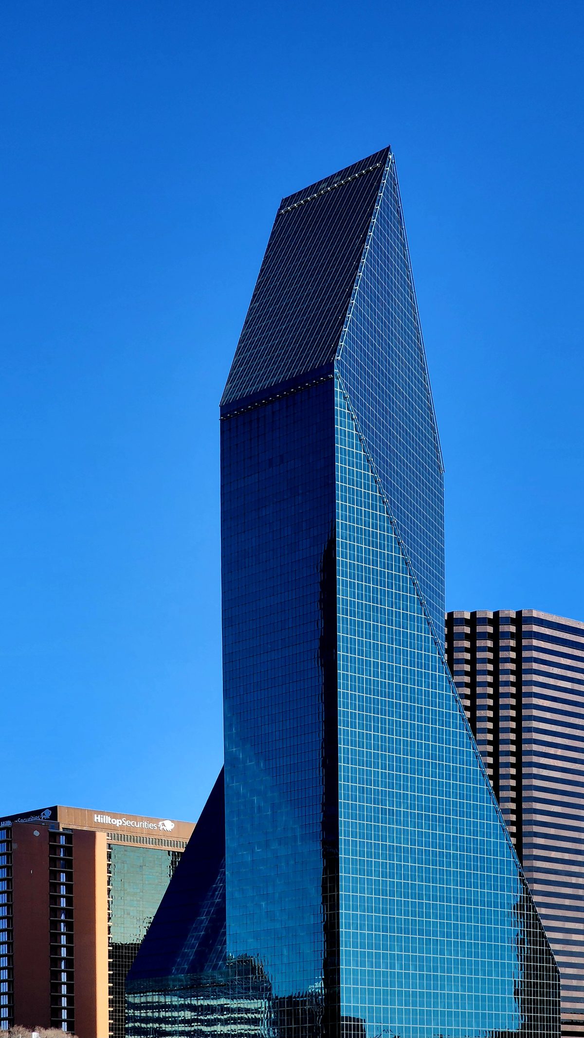 A faceted green glass skyscraper against a deep blue sky in Dallas