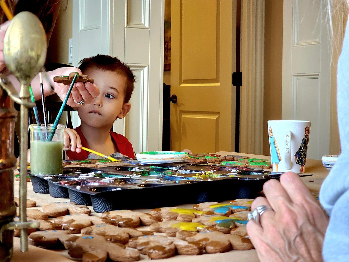 A young boy paints Christmas cookies at the kitchen table