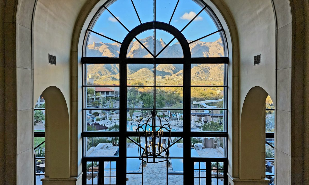A desert resort view through an iron-framed arched window
