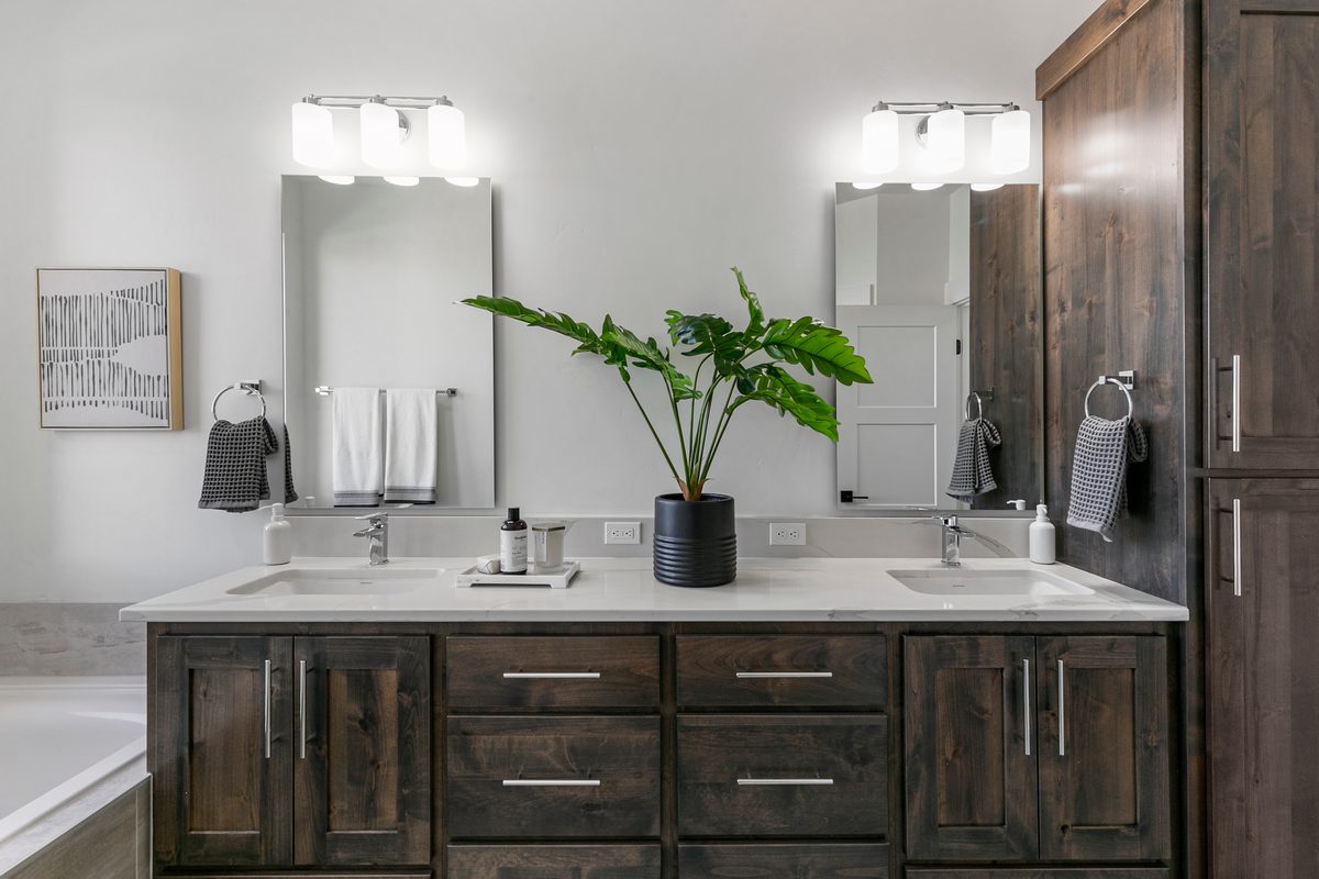 Bathroom with a white double vanity, dark wood cabinets, two mirrors and a potted plant.