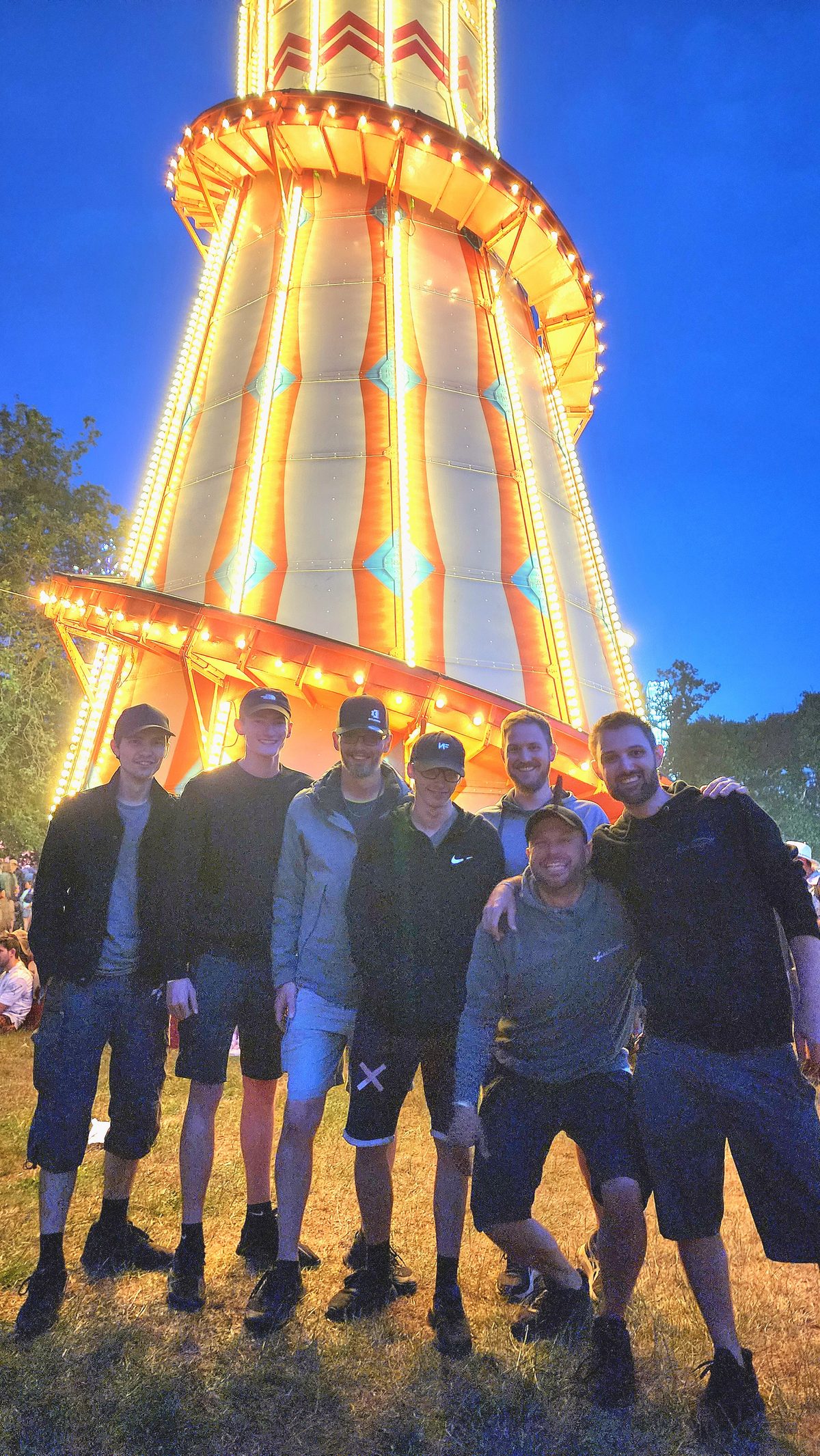 A drone show crew standing in front of a lit fairground helter skelter at night