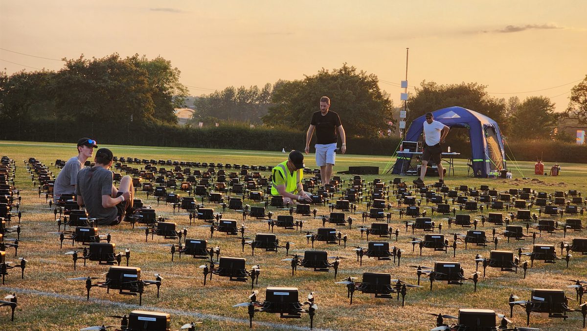 Crew placing hundreds of drones in a grid on a field at golden hour