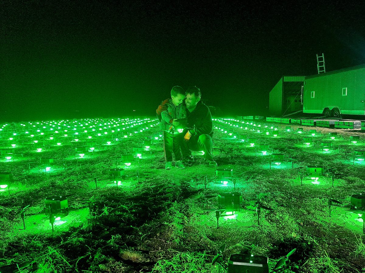 The drone show pilot crouching among hundreds of glowing green drones on a field at night
