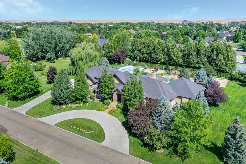 Drone photo of a large home on wooded acreage with a circular driveway and lawn