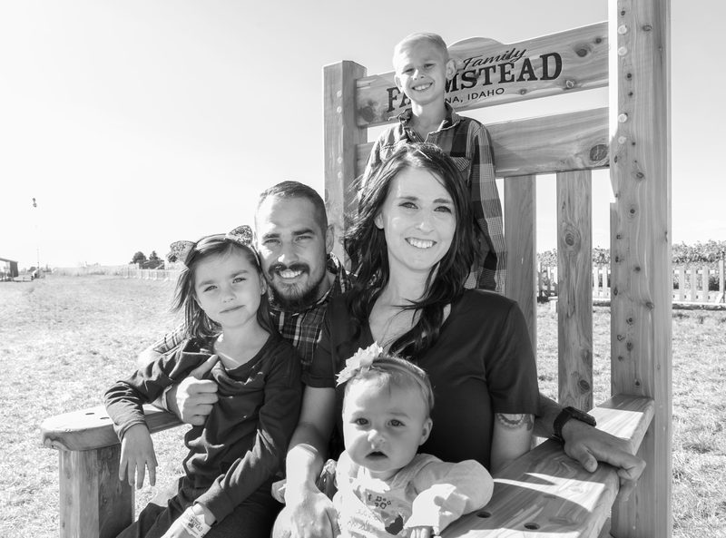 Black-and-white family portrait of two parents and three young children on a wooden bench under a homestead sign