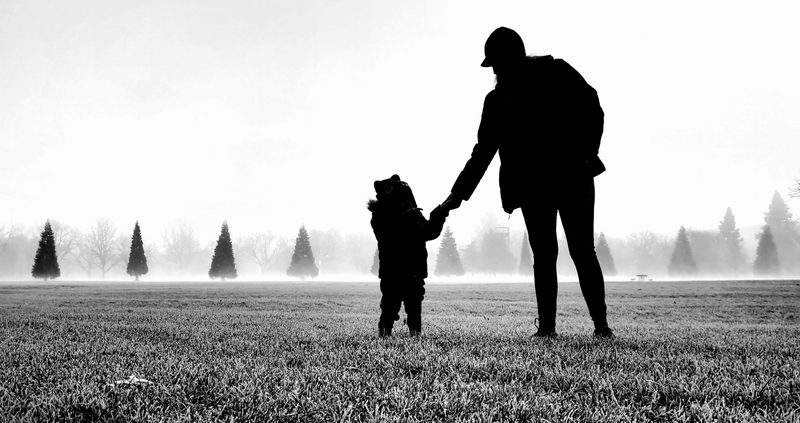 Black-and-white silhouette of a father holding his young son's hand in a foggy field