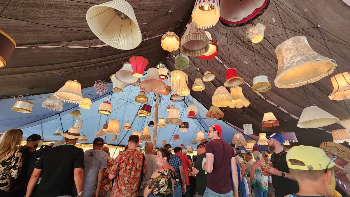 Hundreds of colorful lampshades hanging from a festival tent ceiling over a crowd