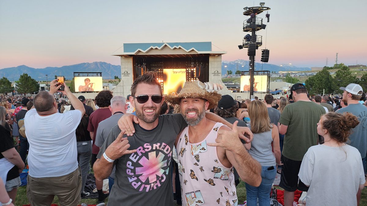 Two friends grinning in a festival crowd in front of a stage