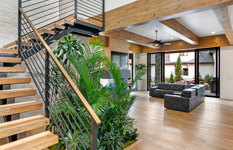Open-tread wood staircase with a cable railing and indoor plants beside a bright open living room