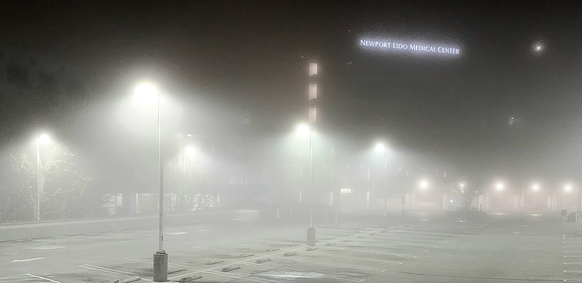 Street lights glowing through thick fog over a parking lot at night