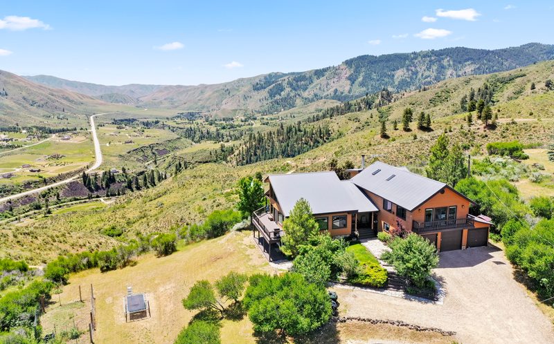 Drone photo of a home set into green foothills with mountain views