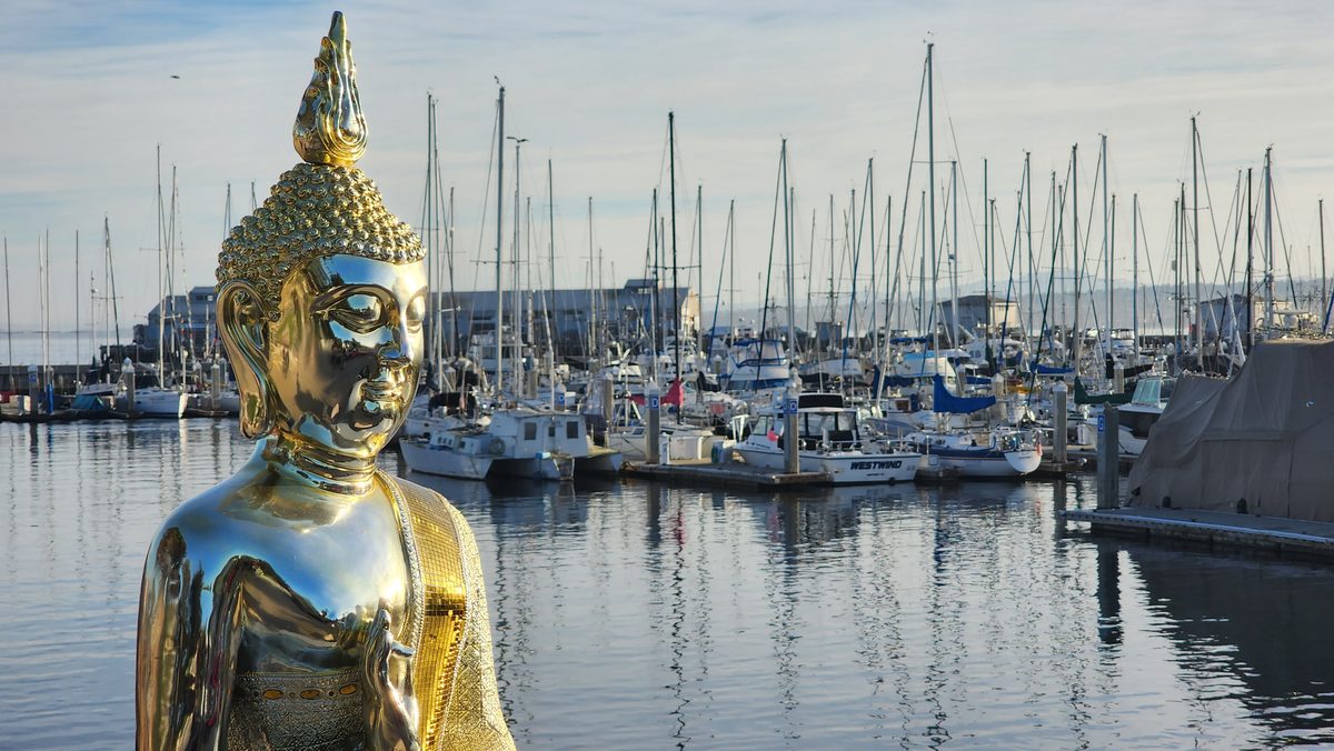 A golden Buddha statue in front of a marina full of sailboats
