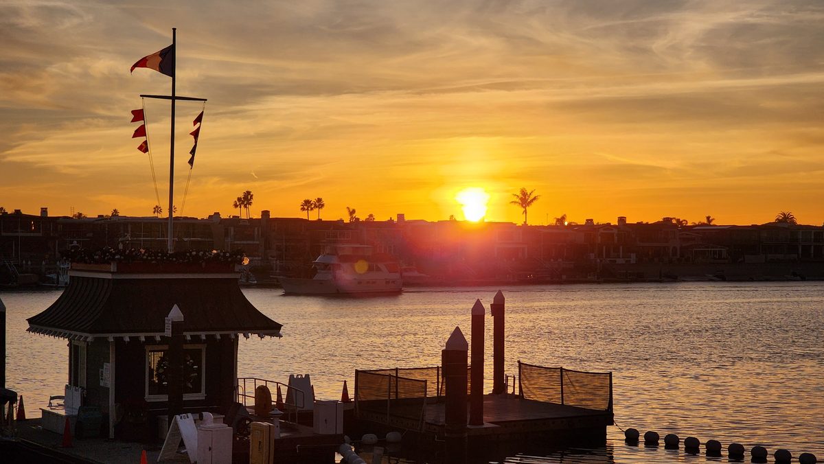 The sun setting over a harbor with a flagpole of nautical signal flags
