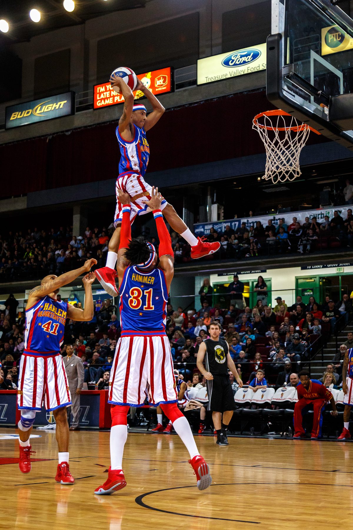 A Harlem Globetrotters player standing on a teammate's shoulders to reach the hoop