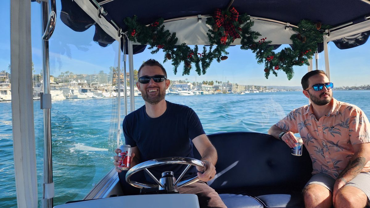 Two men in sunglasses on a garland-decorated boat in the harbor