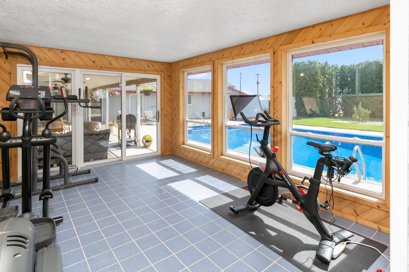 Home gym with a treadmill, exercise bike and large windows looking out to a backyard pool
