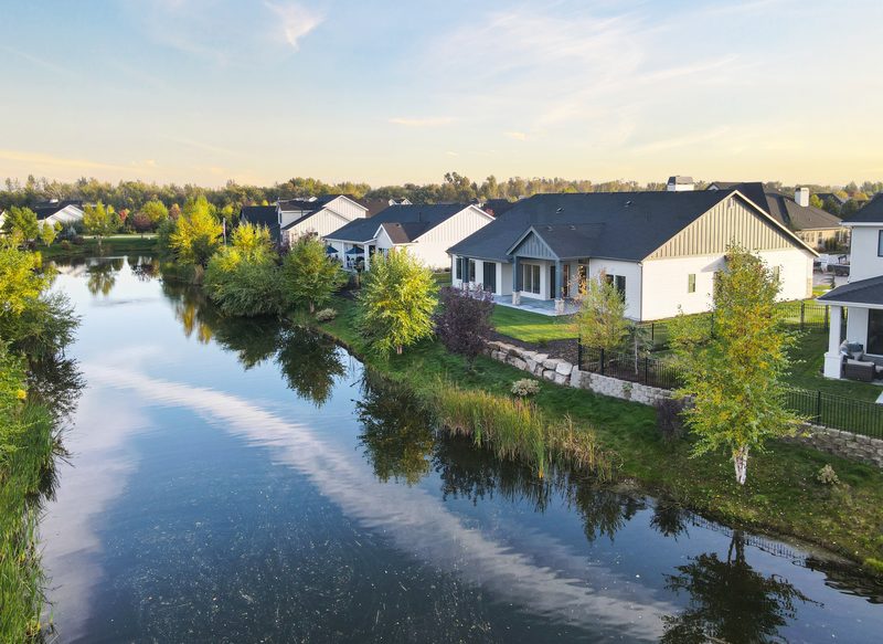 Large white and gray homes line a calm pond that mirrors the sky and trees.