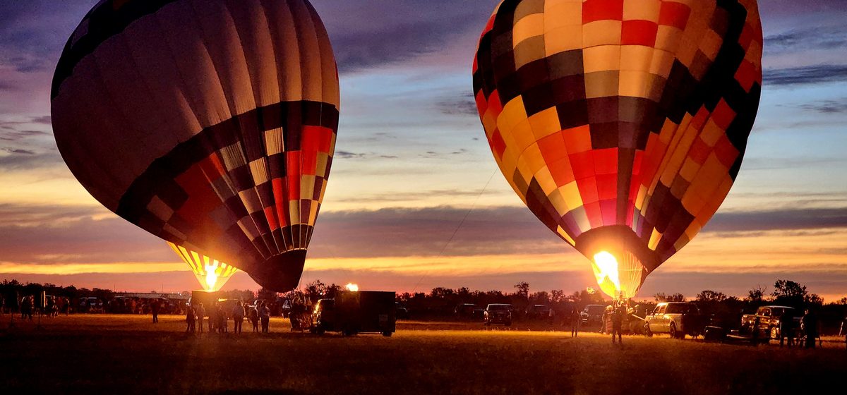 Two hot air balloons glowing as they inflate at dusk