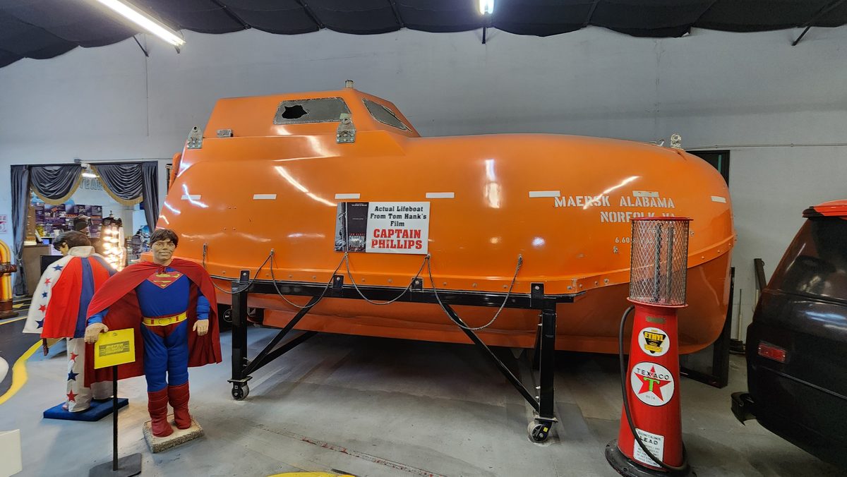 A giant orange hot-dog-shaped car on display with a superhero figure