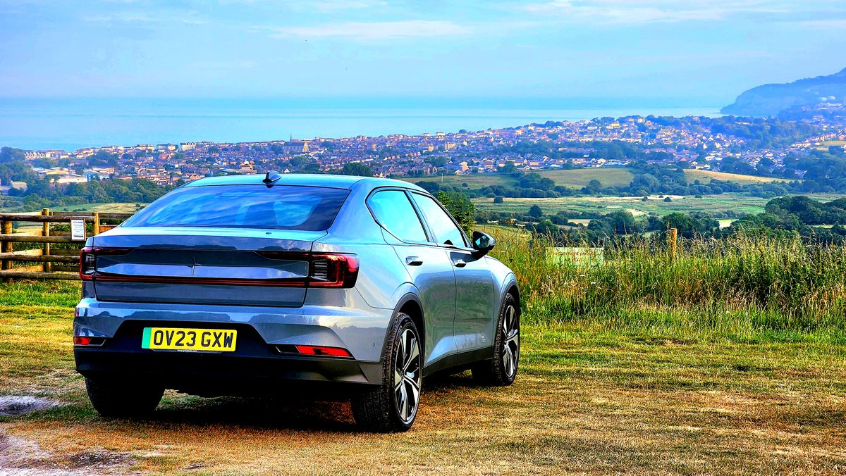 A blue electric car parked at a grassy overlook above the island's towns and sea