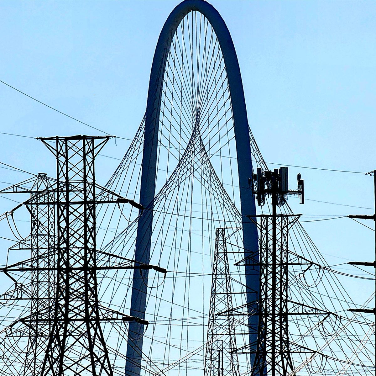 The white arch of the Margaret Hunt Hill Bridge in Dallas behind power lines