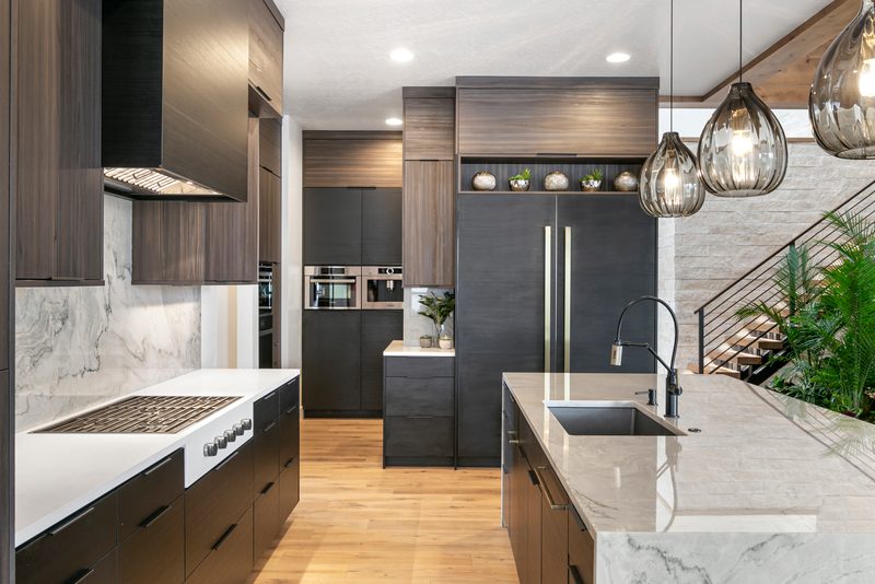 Modern kitchen with dark cabinets, a white marble island, glass pendant lights and a floating staircase