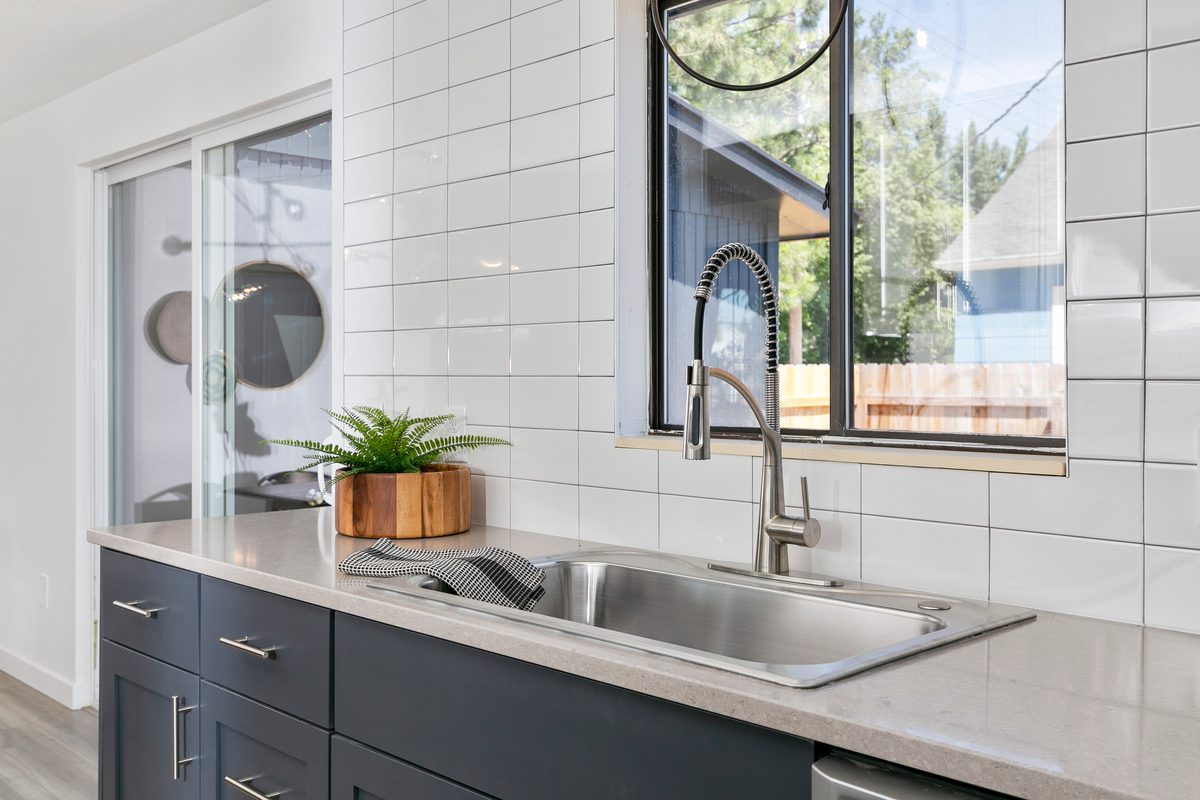 Modern kitchen sink area with gray cabinets, white tile and a window