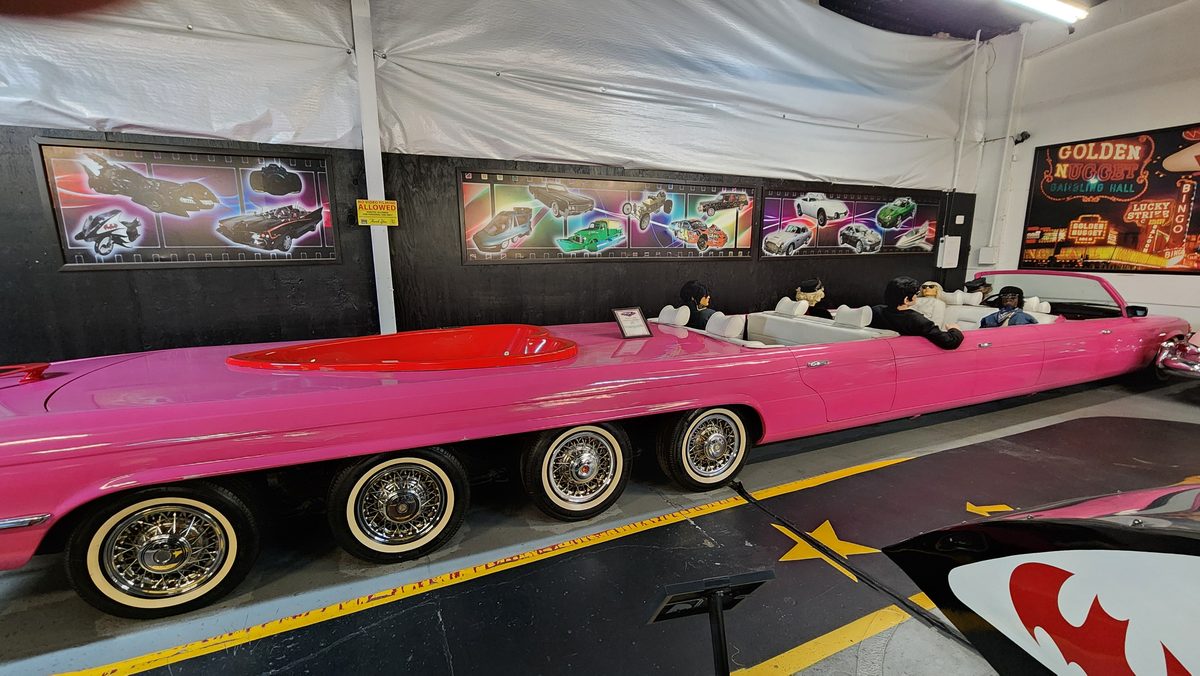 A long pink stretch showcar on display in a car museum