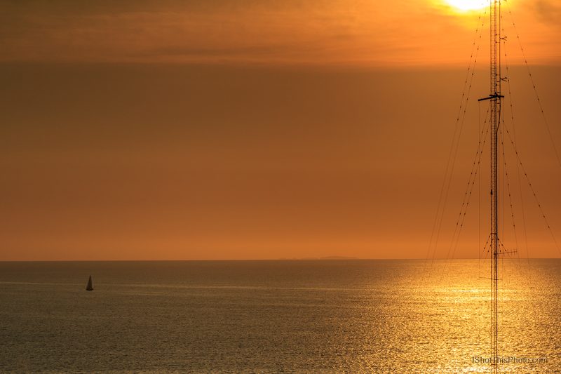 Golden sunset over the Bay of Banderas with a lone sailboat and radio mast in Puerto Vallarta