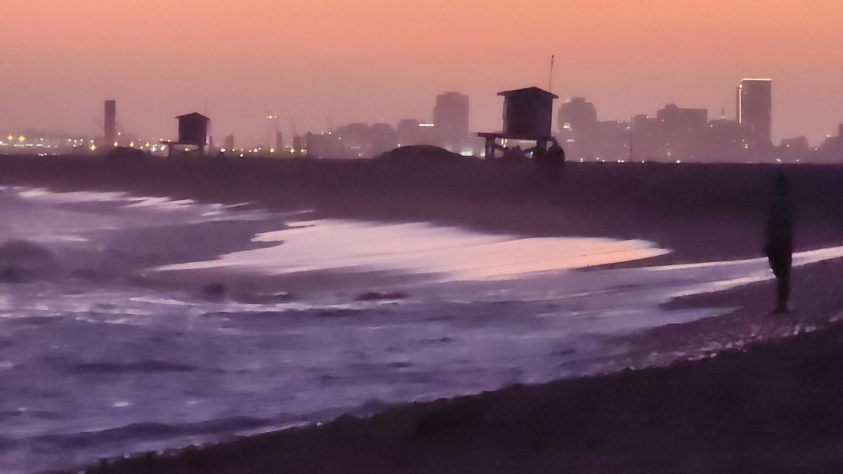 A walker on a beach under a purple and pink dusk sky