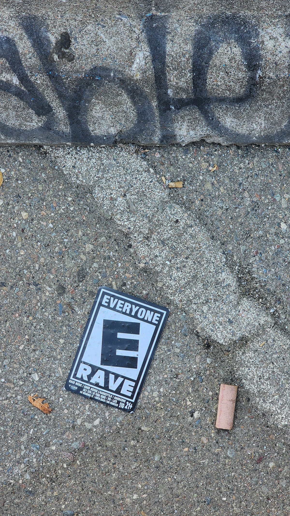 A small rave sticker on a pavement with graffiti