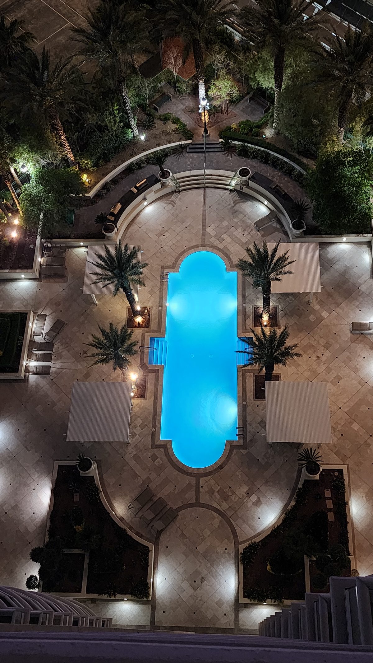 A glowing resort pool and palm courtyard seen from above at night
