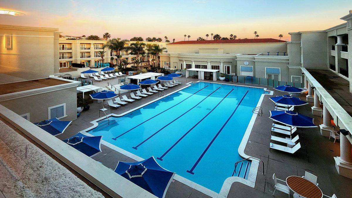 A blue resort pool with loungers and harbor views at sunset