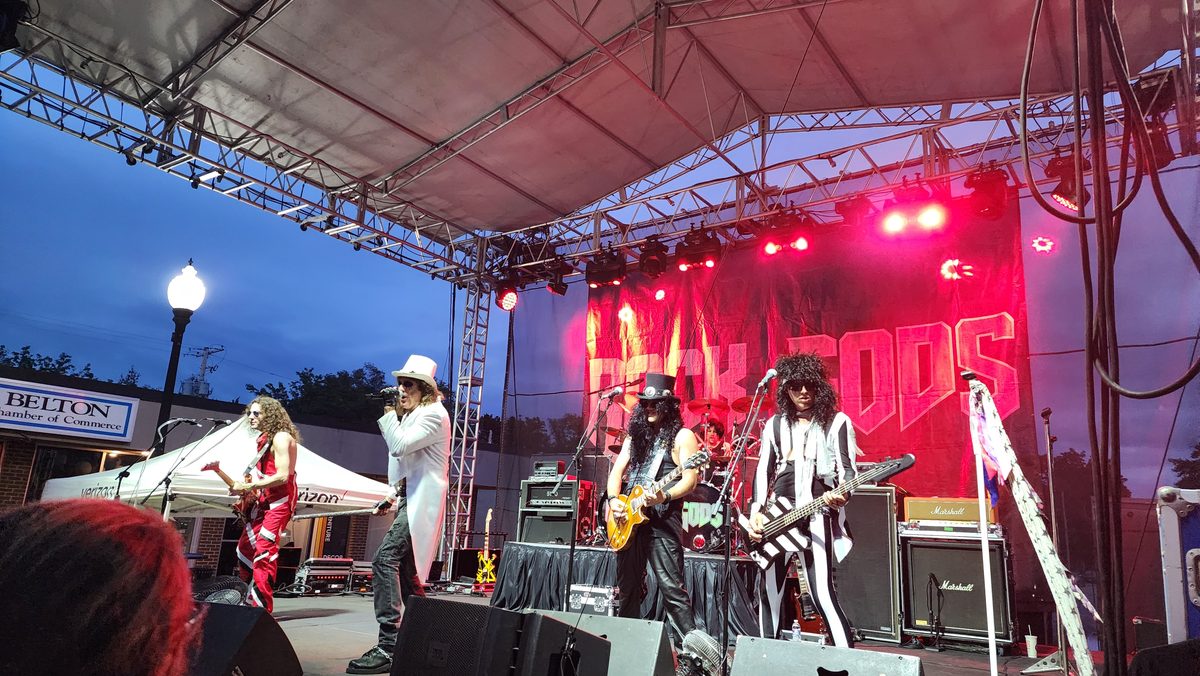 A rock band playing under red stage lights at an outdoor show