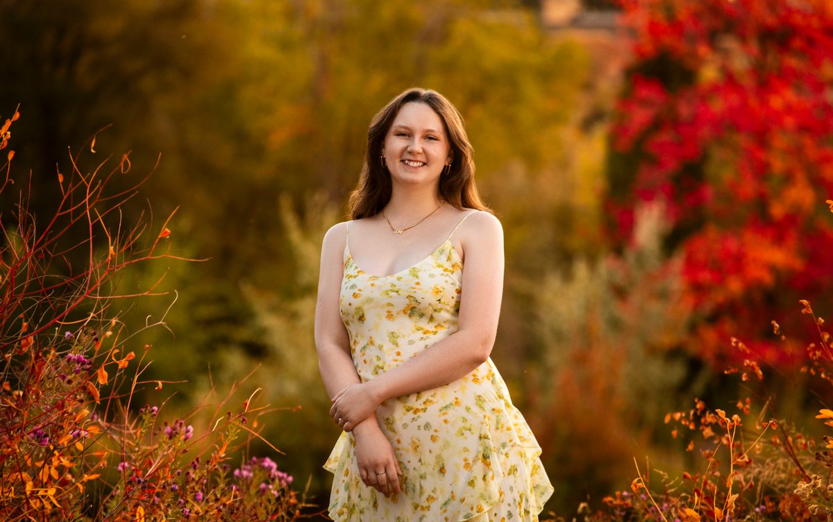 Smiling senior girl in a yellow sundress surrounded by red and gold fall foliage