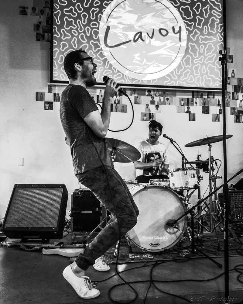 Black-and-white photo of a singer leaning back from the mic in front of a drummer on a small stage