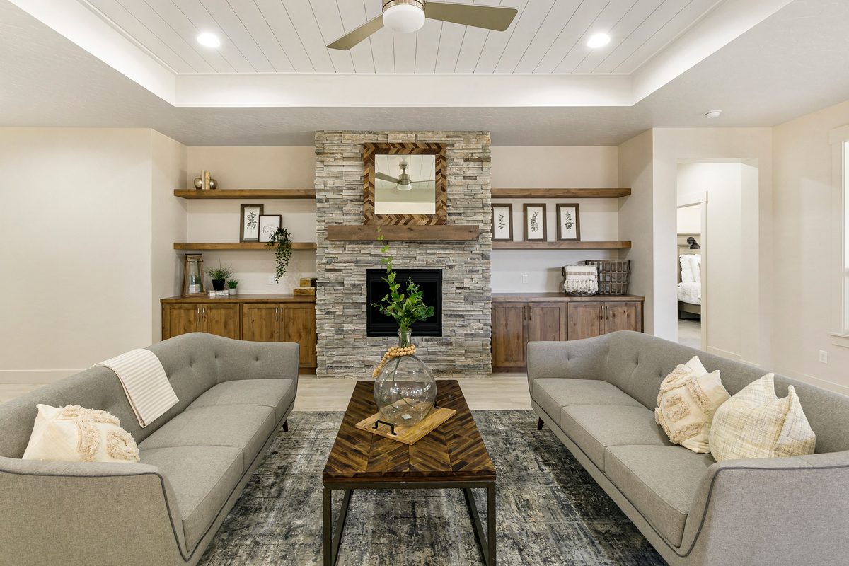 Staged living room with two sofas facing a stacked-stone fireplace and built-in shelves