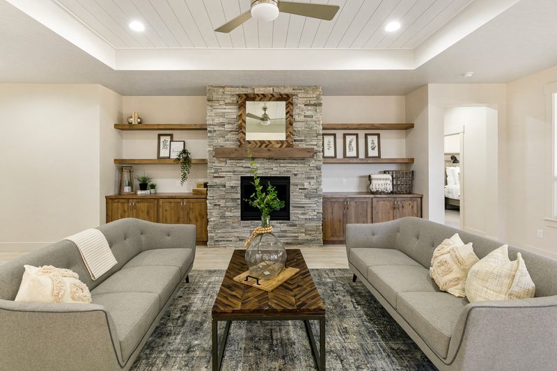 Staged living room with two sofas facing a stacked-stone fireplace and built-in shelves