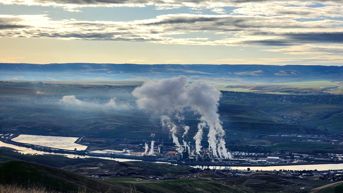 White steam plumes rising from a plant in a wide valley under a cloudy sky