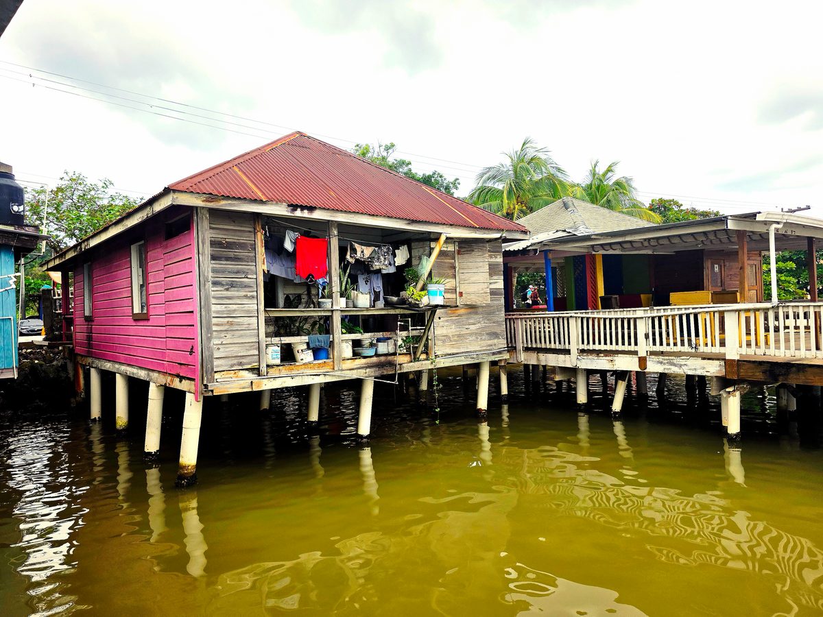 Colorful wooden houses on stilts above green river water, with laundry hanging on a porch